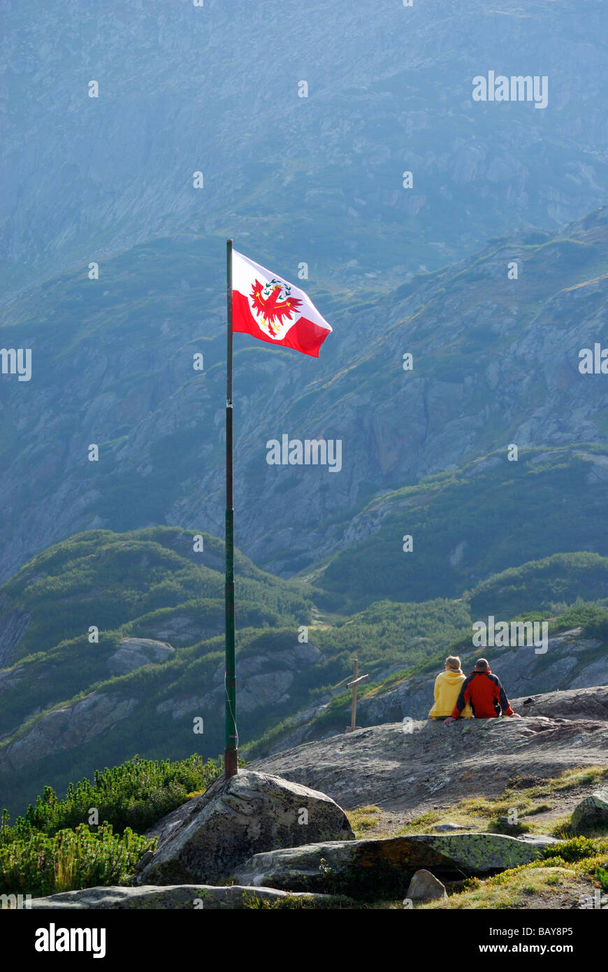 couple beneath Tyrolean flag, hut Sulzenauhuette, Stubaier Alpen range, Stubai, Tyrol, Austria Stock Photo