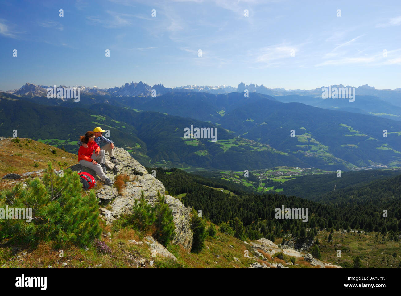 couple sitting on rim with view to valley of Eisack and to Dolomites with Peitlerkofel, Geislergruppe, Sella, Langkofelgruppe an Stock Photo