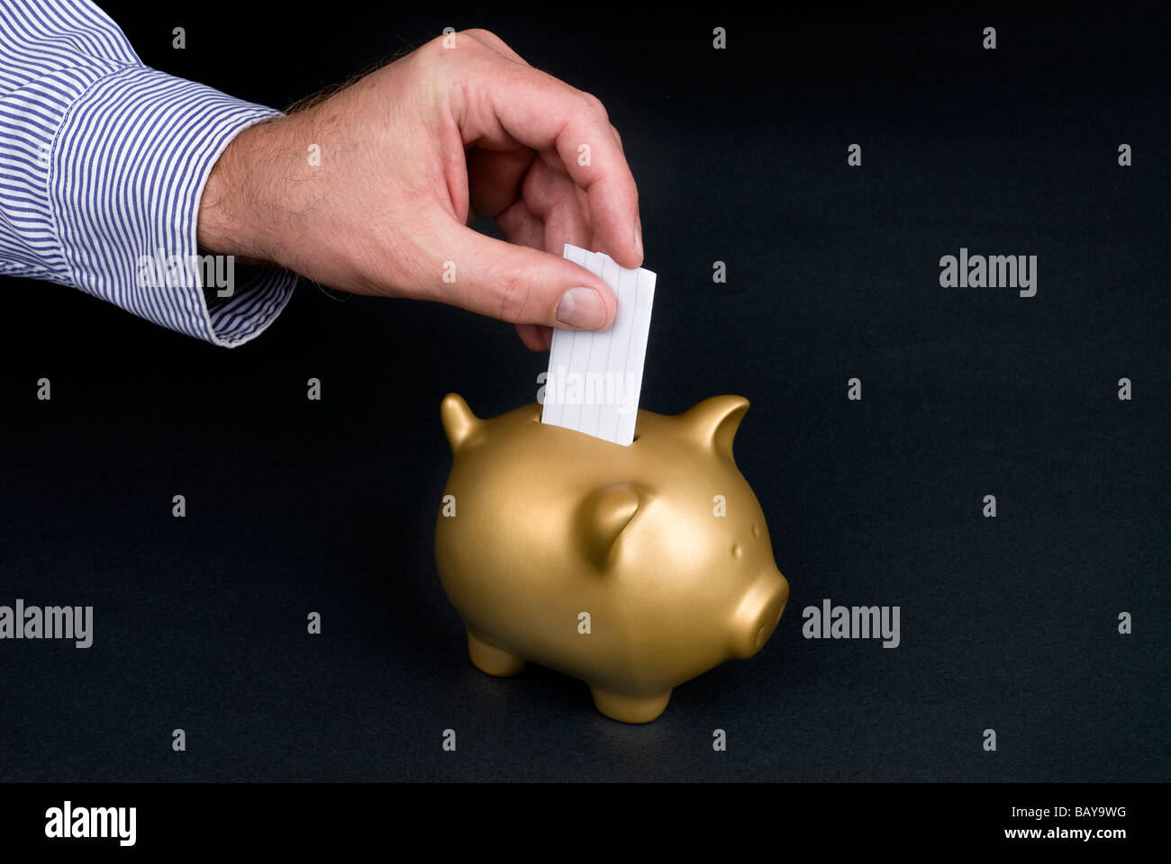 A man places a slip of paper into a piggy bank with copy space Stock Photo
