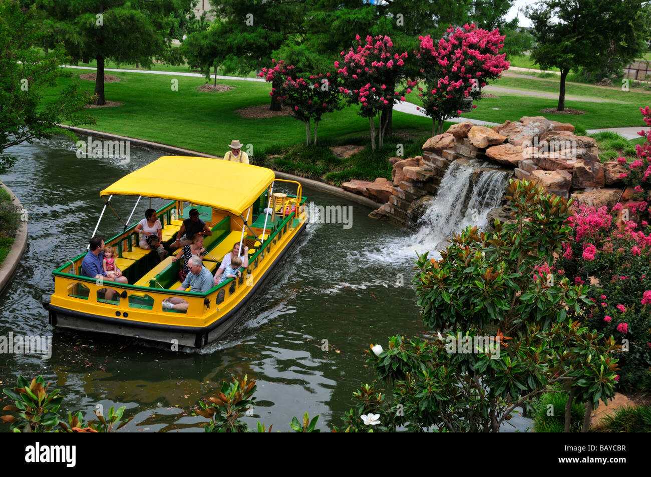 A water taxi cruises past flowers and a small waterfall in Bricktown, Oklahoma City Stock Photo