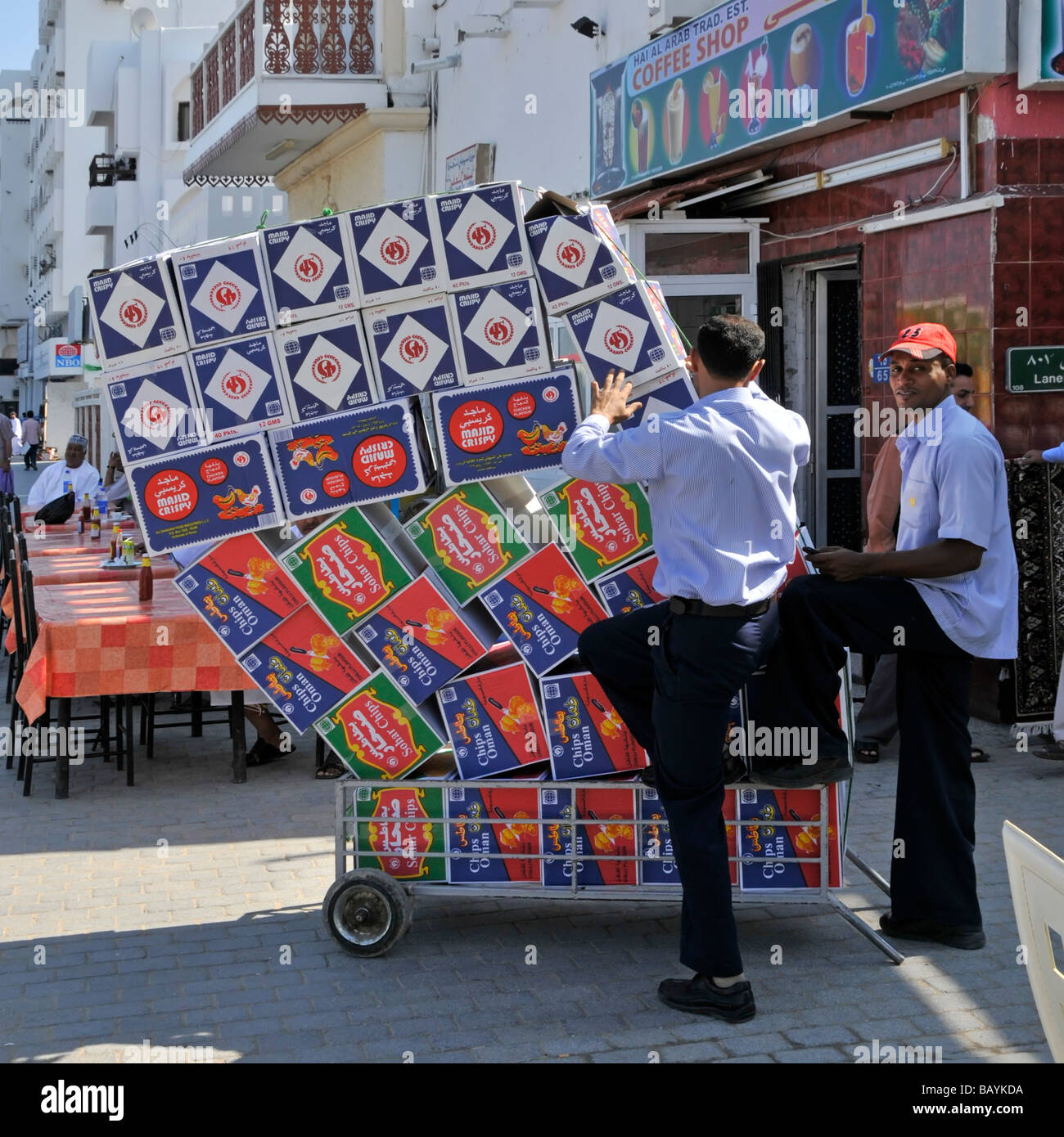 Street scene cafe workers wheeling trolley loaded with boxes of chips after unloading delivery vehicle Muttrah Muscat Oman Arabian Sea Gulf of Oman Stock Photo