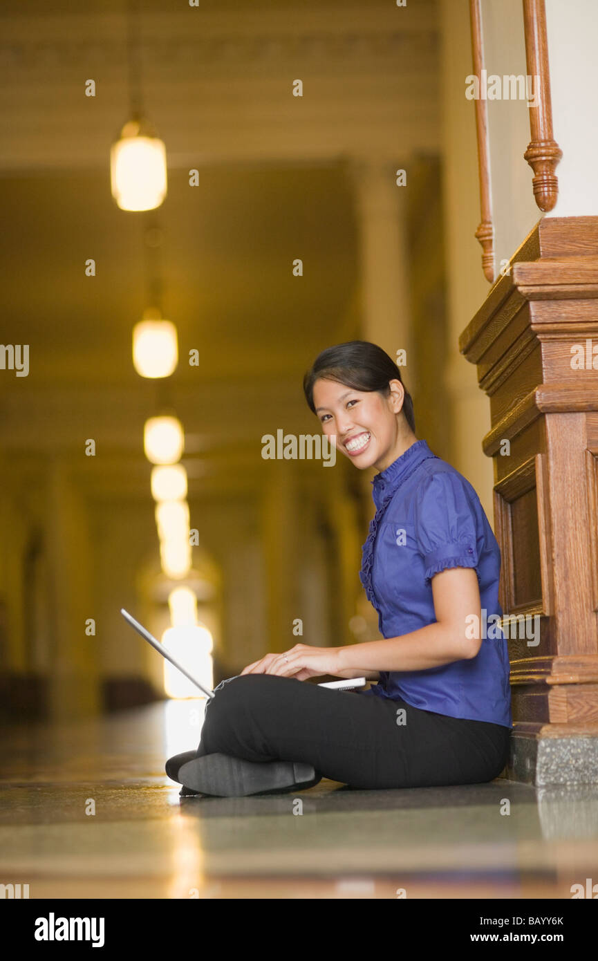 African woman typing on laptop in corridor Stock Photo