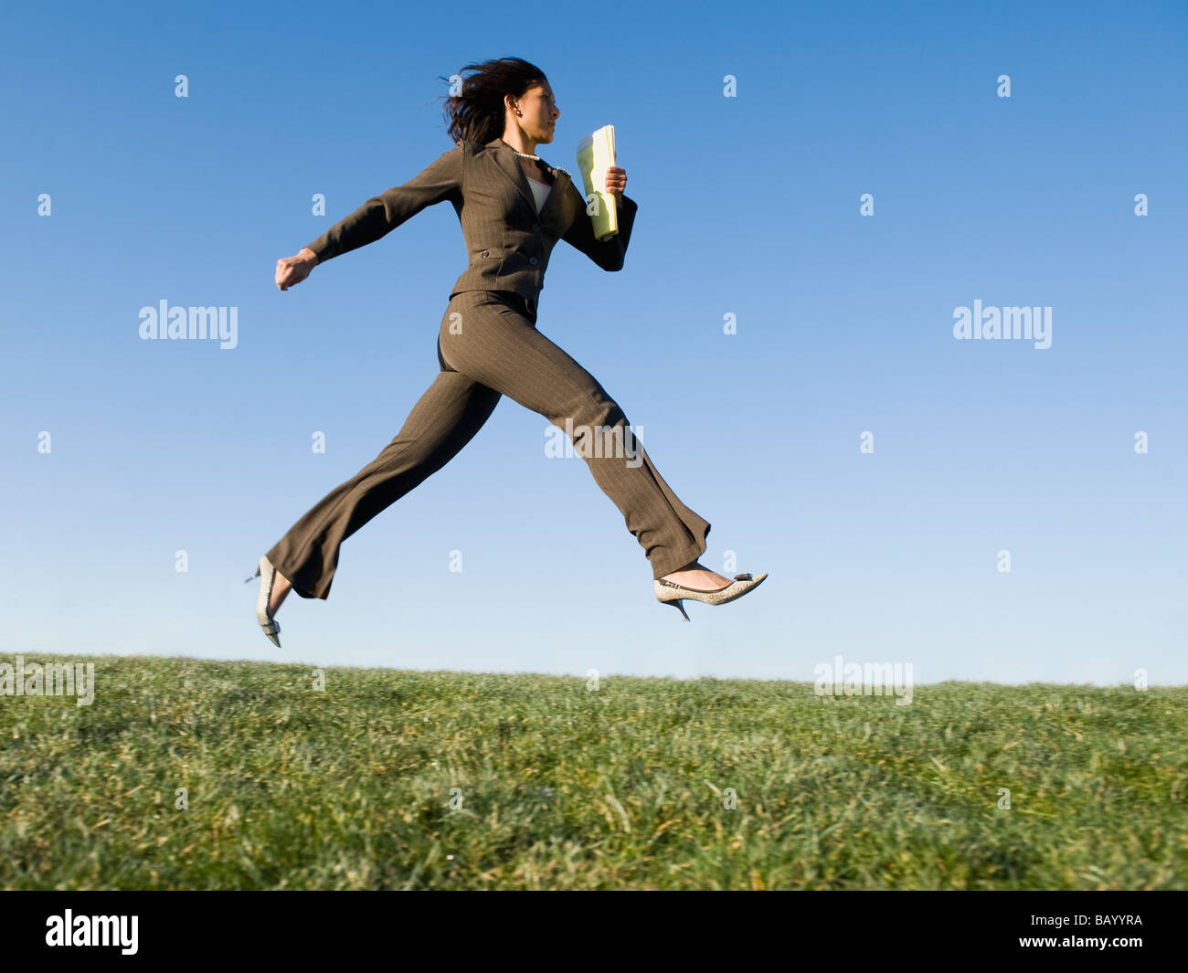 Mixed race businesswoman leaping in field Stock Photo
