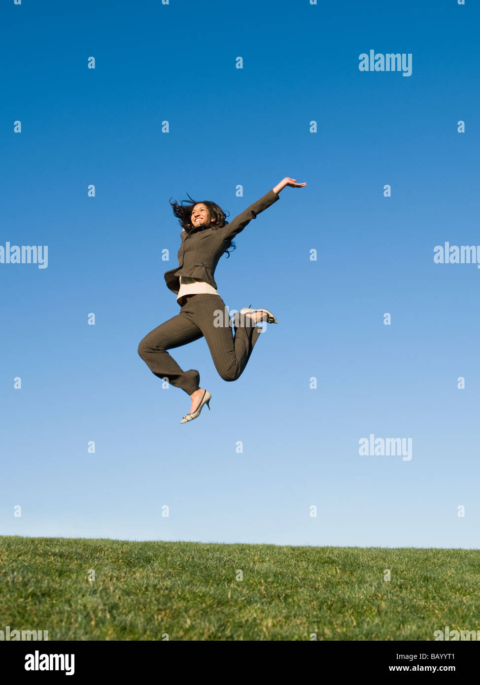 Mixed race businesswoman jumping in field Stock Photo