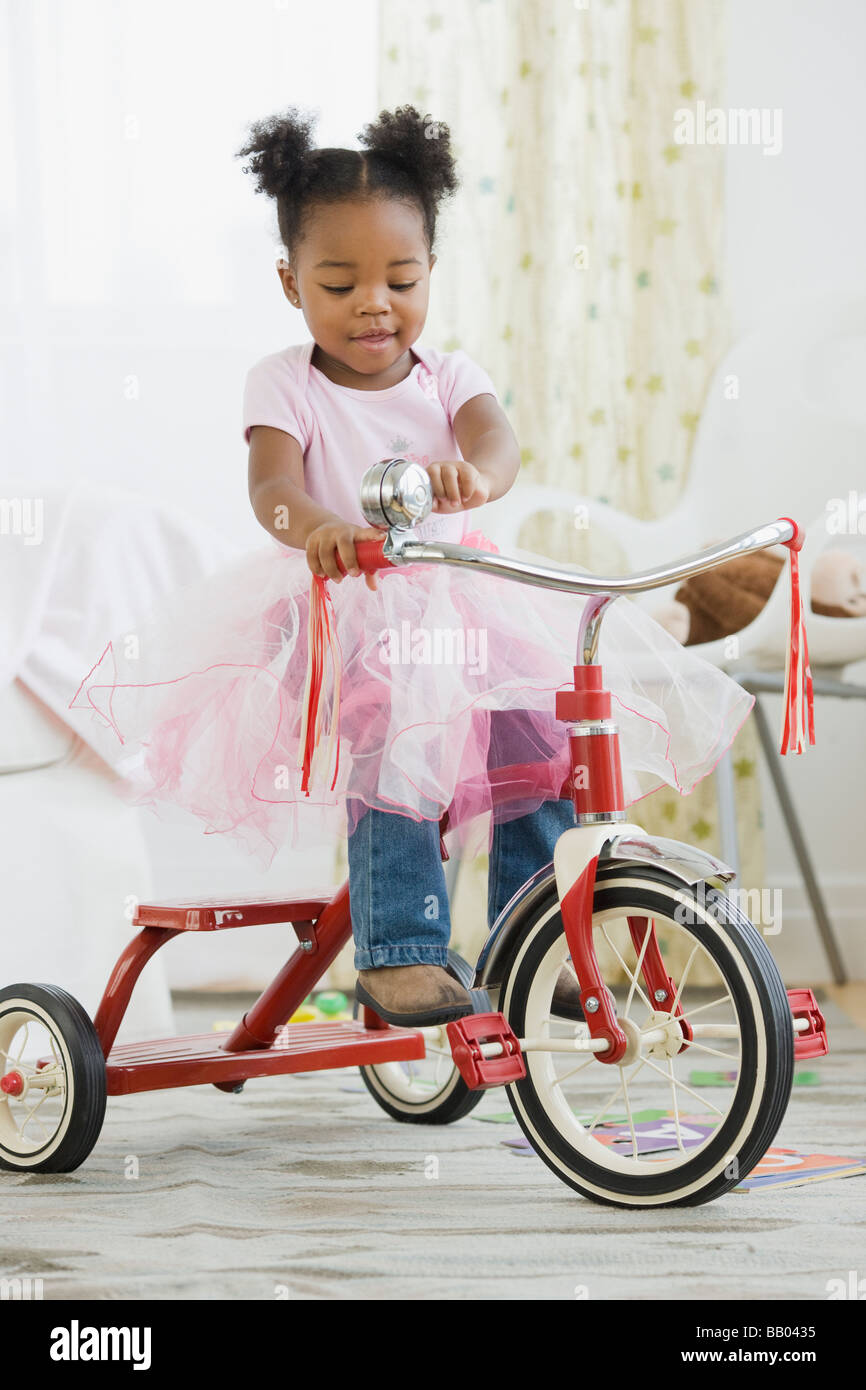 African American girl in costume riding tricycle Stock Photo