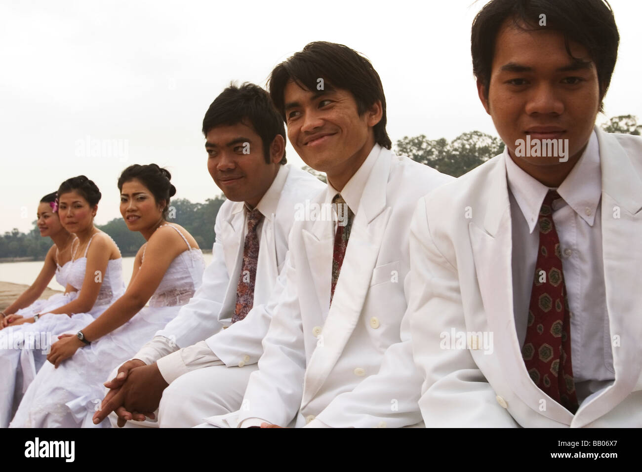 A wedding party sits by while the bride and groom are photographed at