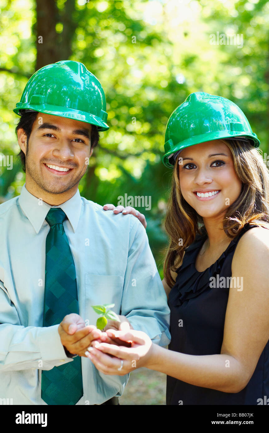 Hispanic business people with green hard hats holding tree sprout Stock