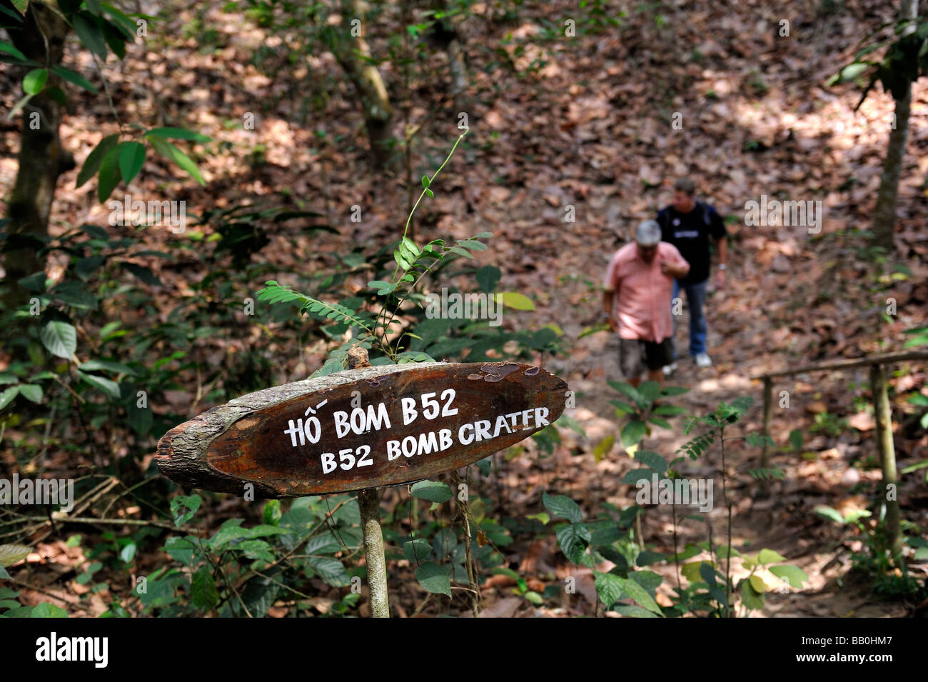 Men in a B52 bomb crater from the Vietnam War (known as the American War in Vietnam) with hand painted sign. Cu Chi, Vietnam Stock Photo