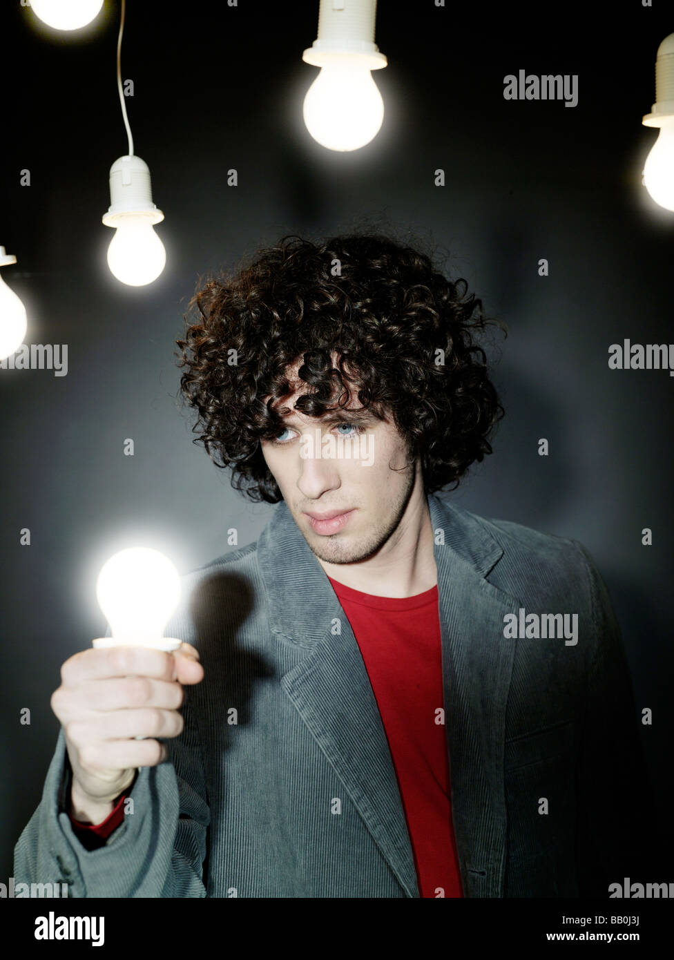 1251741 people man 20 25 curly dark haired light bulb bulbs hold indoor vertical Stock Photo