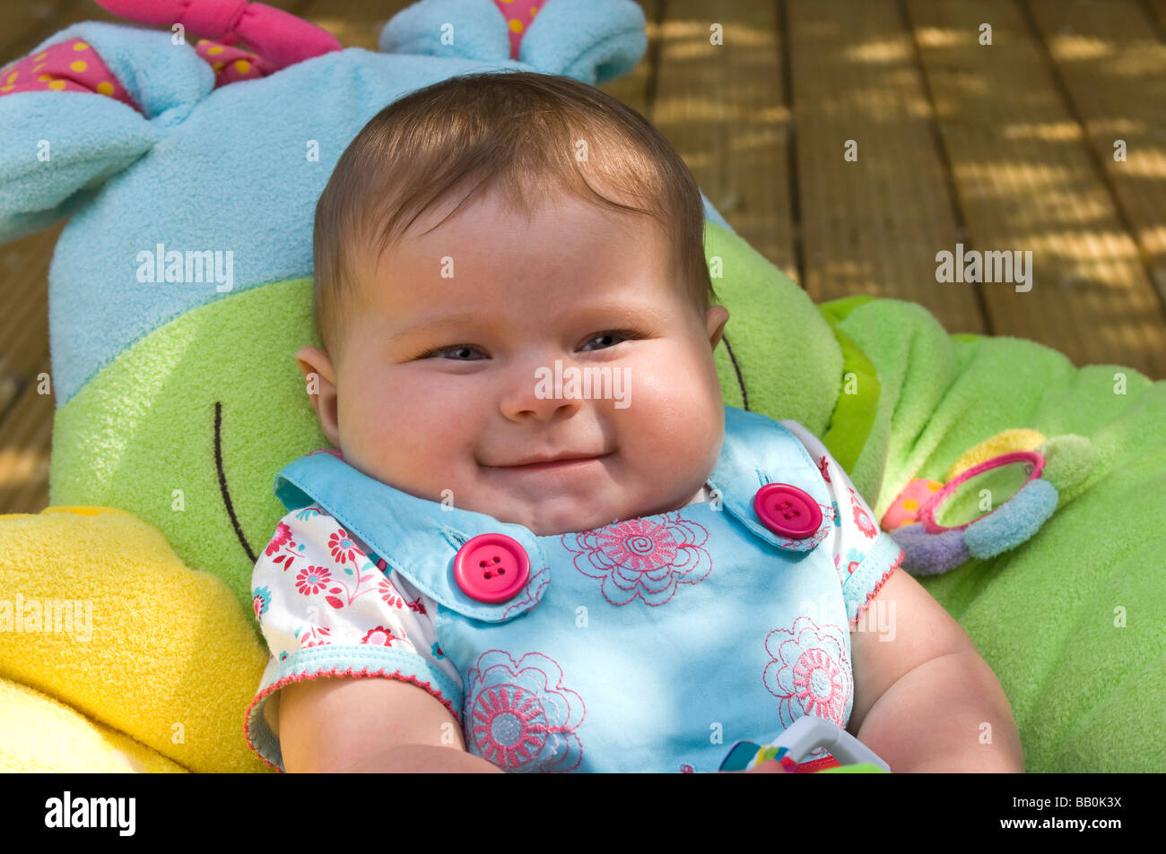 Horizontal close up portrait of a six month old baby girl shrugging her shoulders laughing in the garden on a sunny day Stock Photo