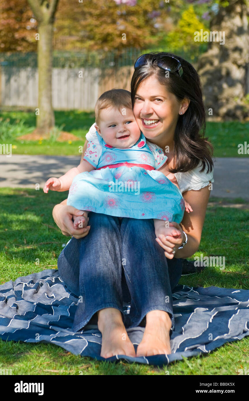 Vertical close up portrait of a young mum playing and tickling her baby daughter's feet making her laugh outside in the sunshine Stock Photo