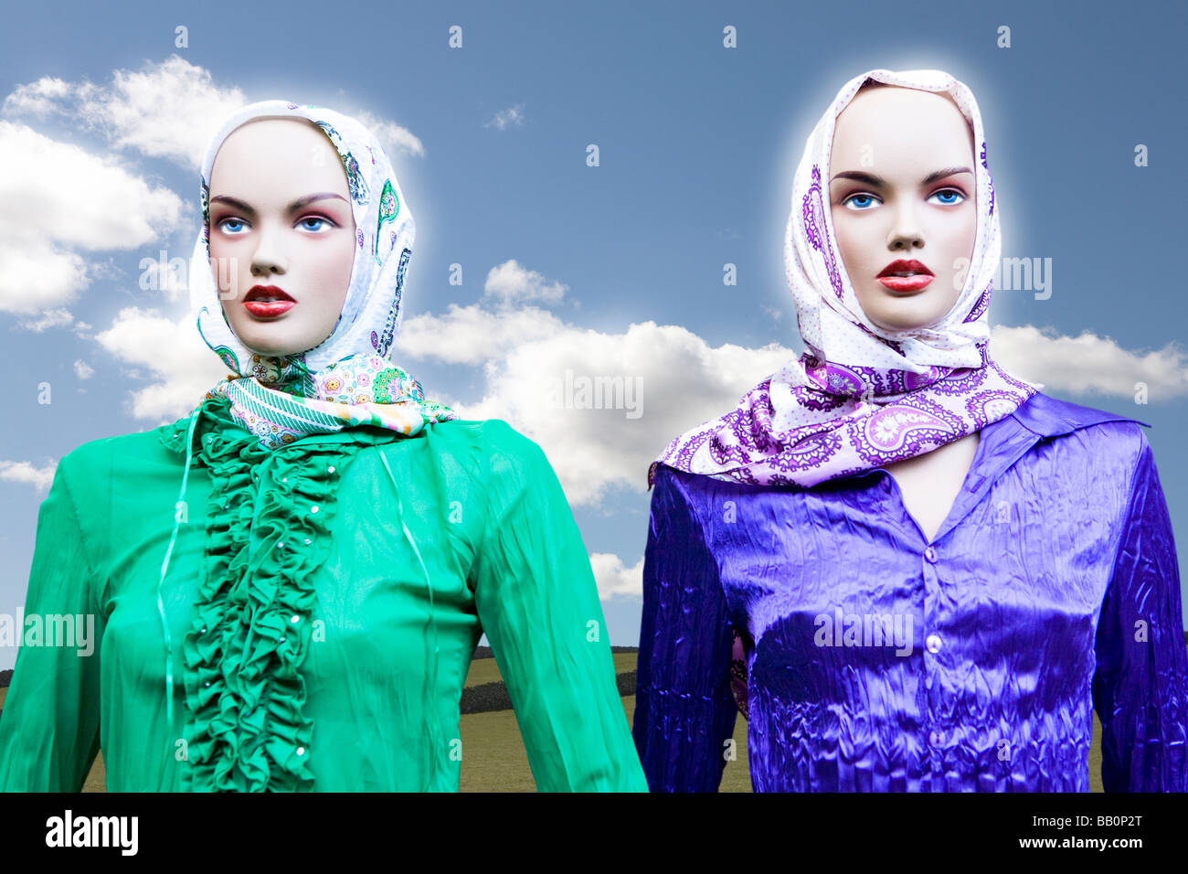 Two female shop window mannequins with head scarves and silk blouses against a country scene and blue sky Stock Photo