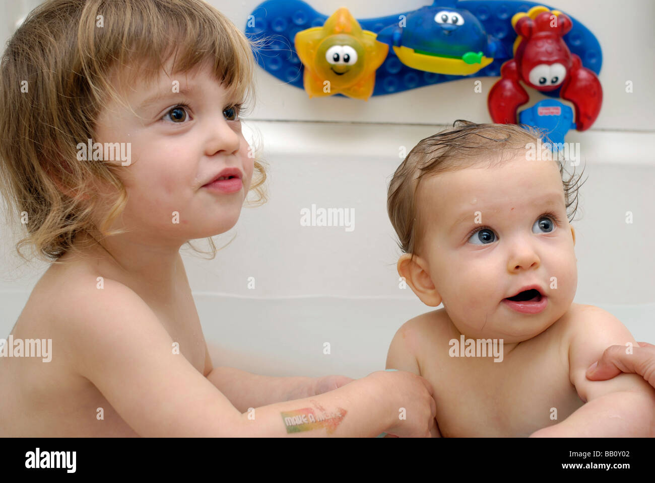Sisters Two and half years and nine months old sharing a bath and looking off camera at their