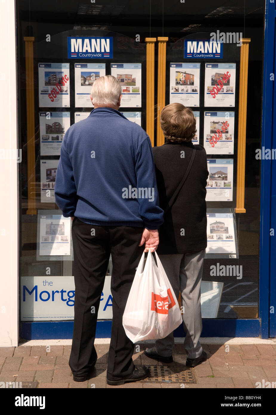 Elderly couple perusing estate agents window of Mann Countrywide, High