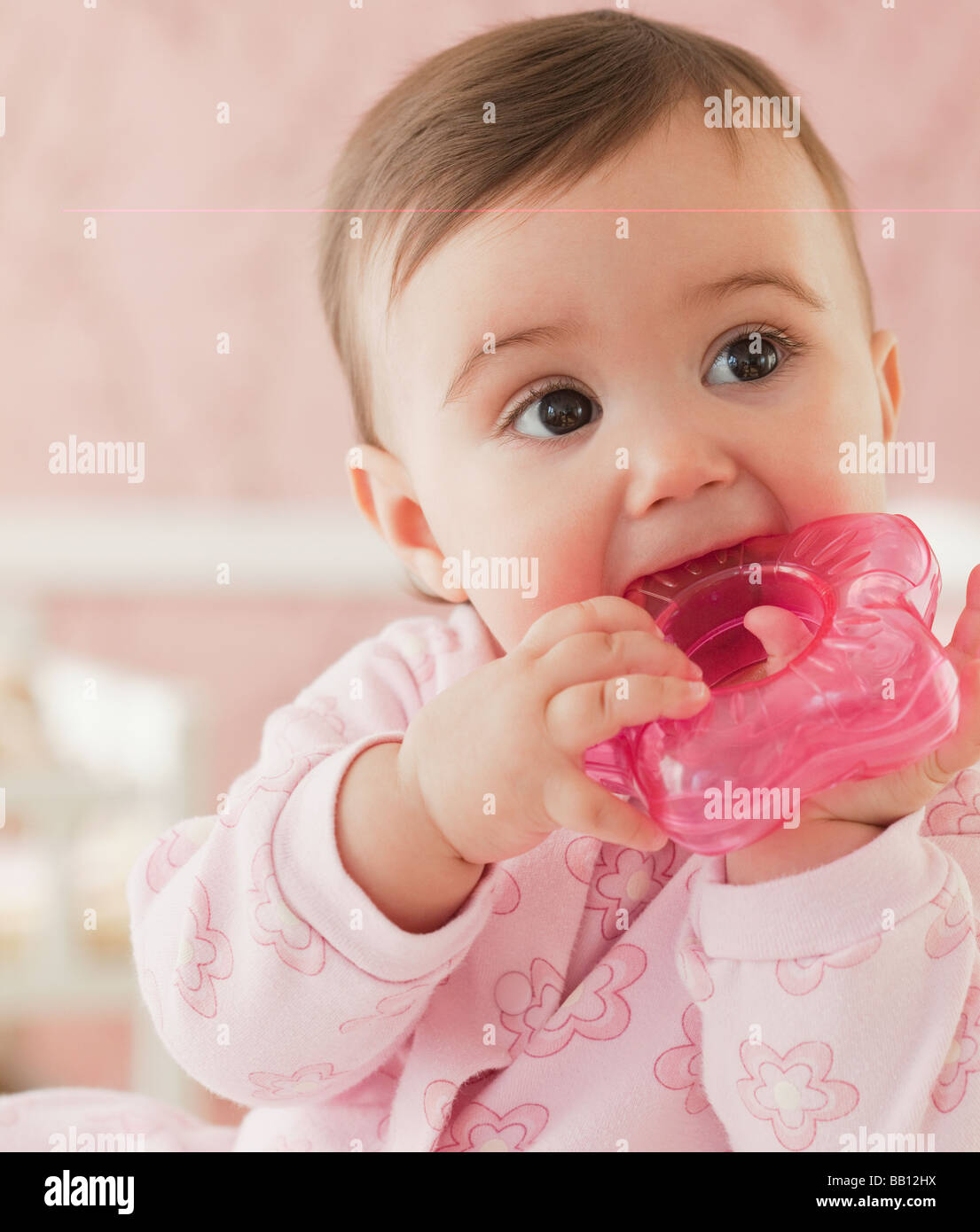 Mixed race baby girl chewing on plastic toy Stock Photo