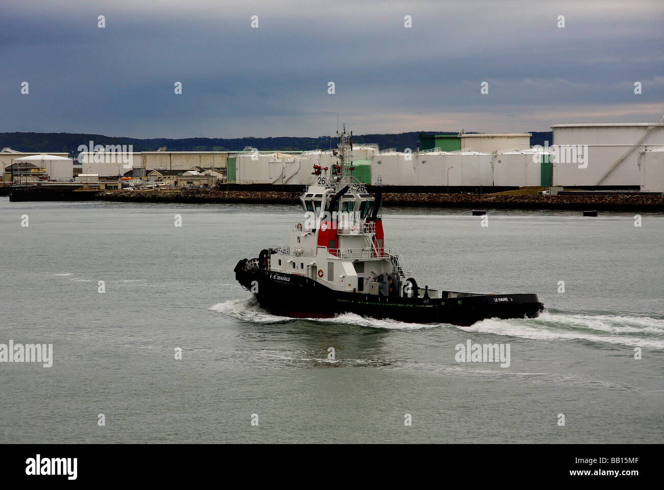 a small tug boat cruising back to Le Havre port under a grey sky containers on the dock side in the background France Stock Photo