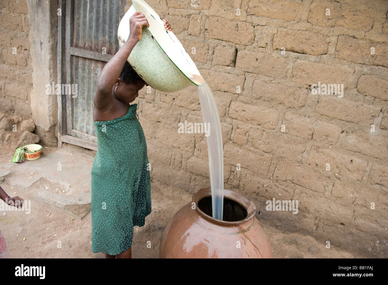 Woman pouring water from large bowl on her head into container, village