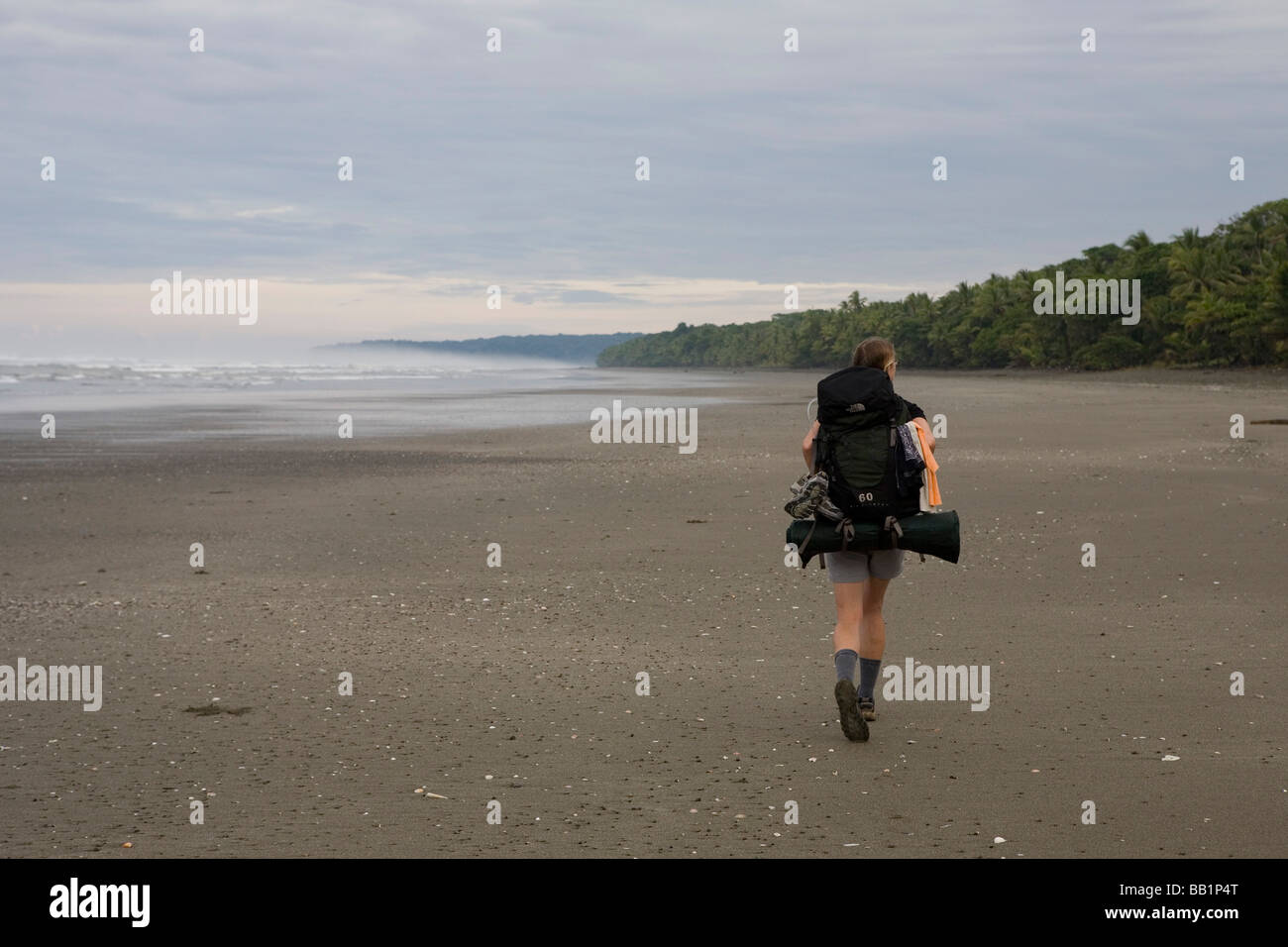 A woman hikes with a backpack along the sandy coastline fo Corcovado National Park, Costa Rica. Stock Photo