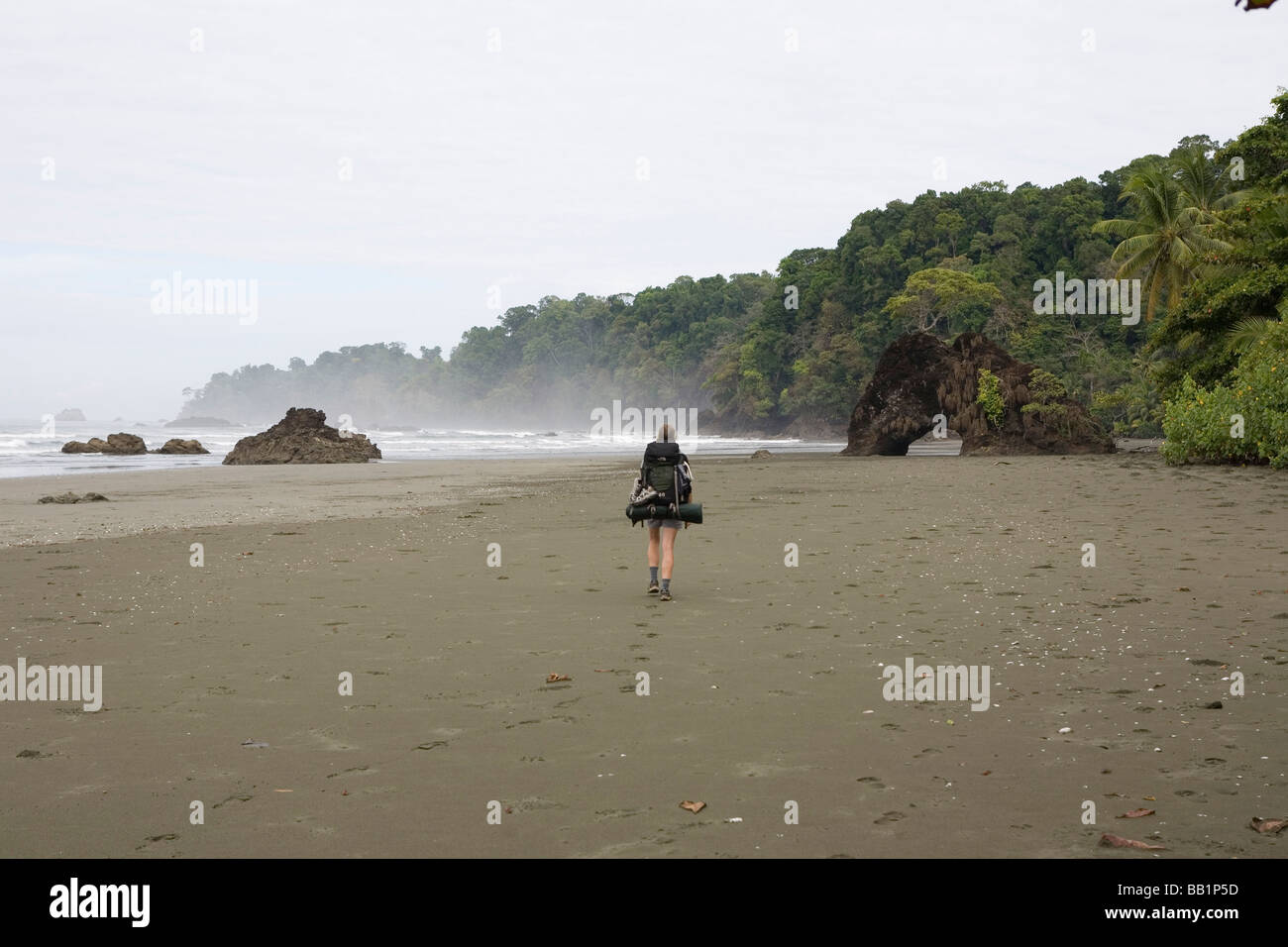 A woman hikes with a backpack along the sandy coastline fo Corcovado National Park, Costa Rica. Stock Photo