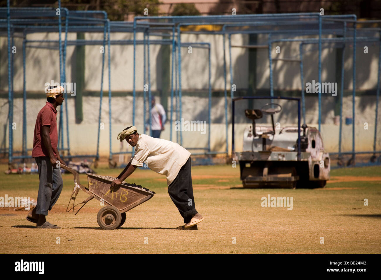 Groundsmen work on the training pitch at the M. Chinnaswamy stadium in Bangalore, India. They push a wheelbarrow onto the field. Stock Photo