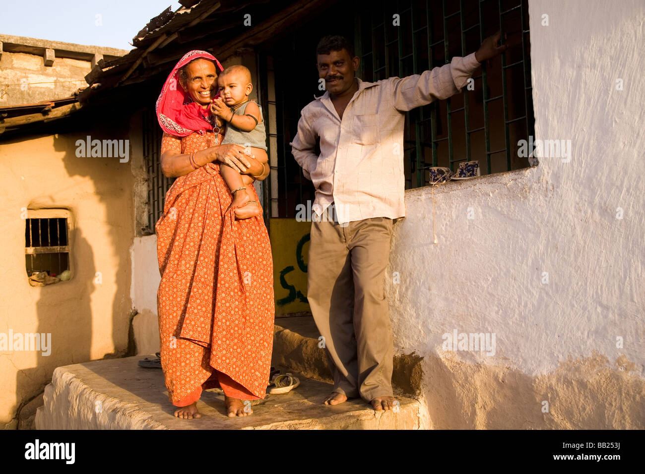 A typical rural house and family in the Gujarati town of Sasan, India. The woman in a red sari holds her grandson. Stock Photo