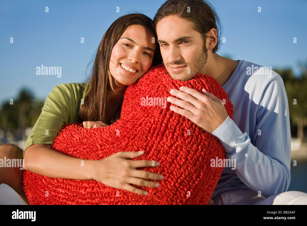 Portrait of a couple hugging a heart shaped cushion Stock Photo - Alamy