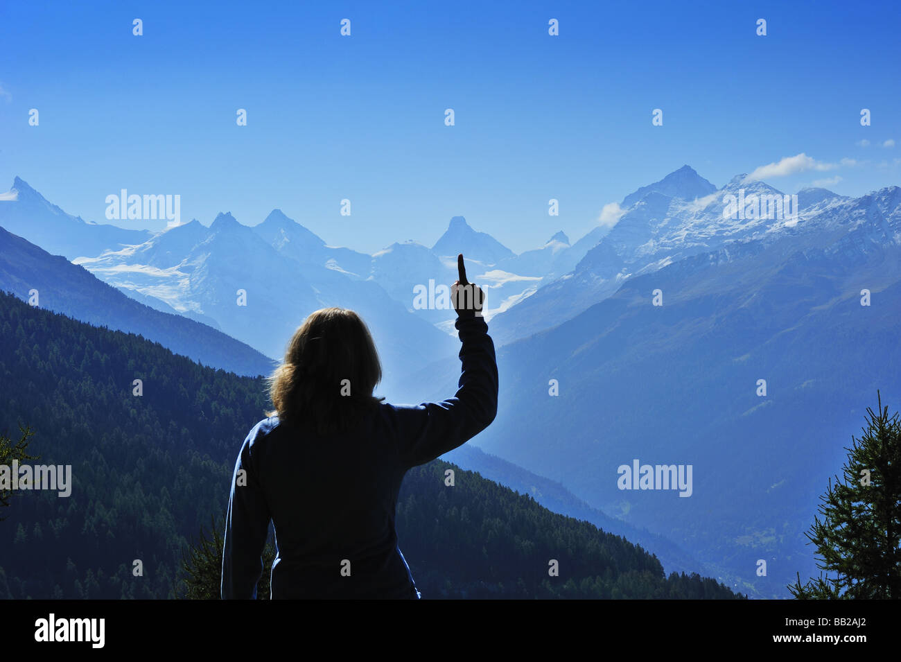 A silhouette of a tourist in the Alps, pointing at the Matterhorn in amongst the distant peaks Stock Photo