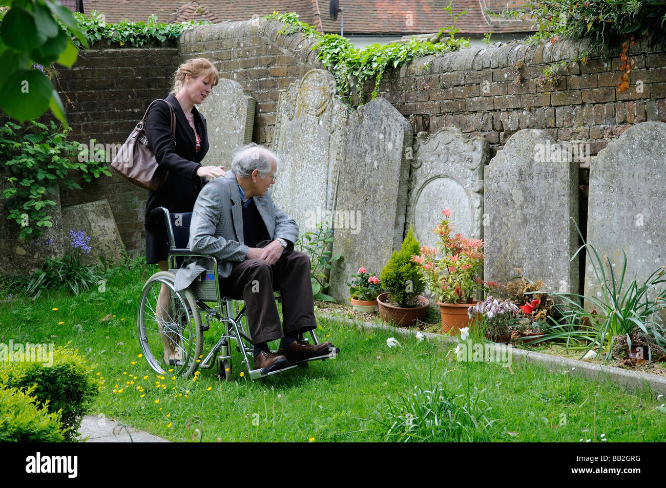 Elderly man in wheelchair being pushed around a graveyard by his female carer Stock Photo