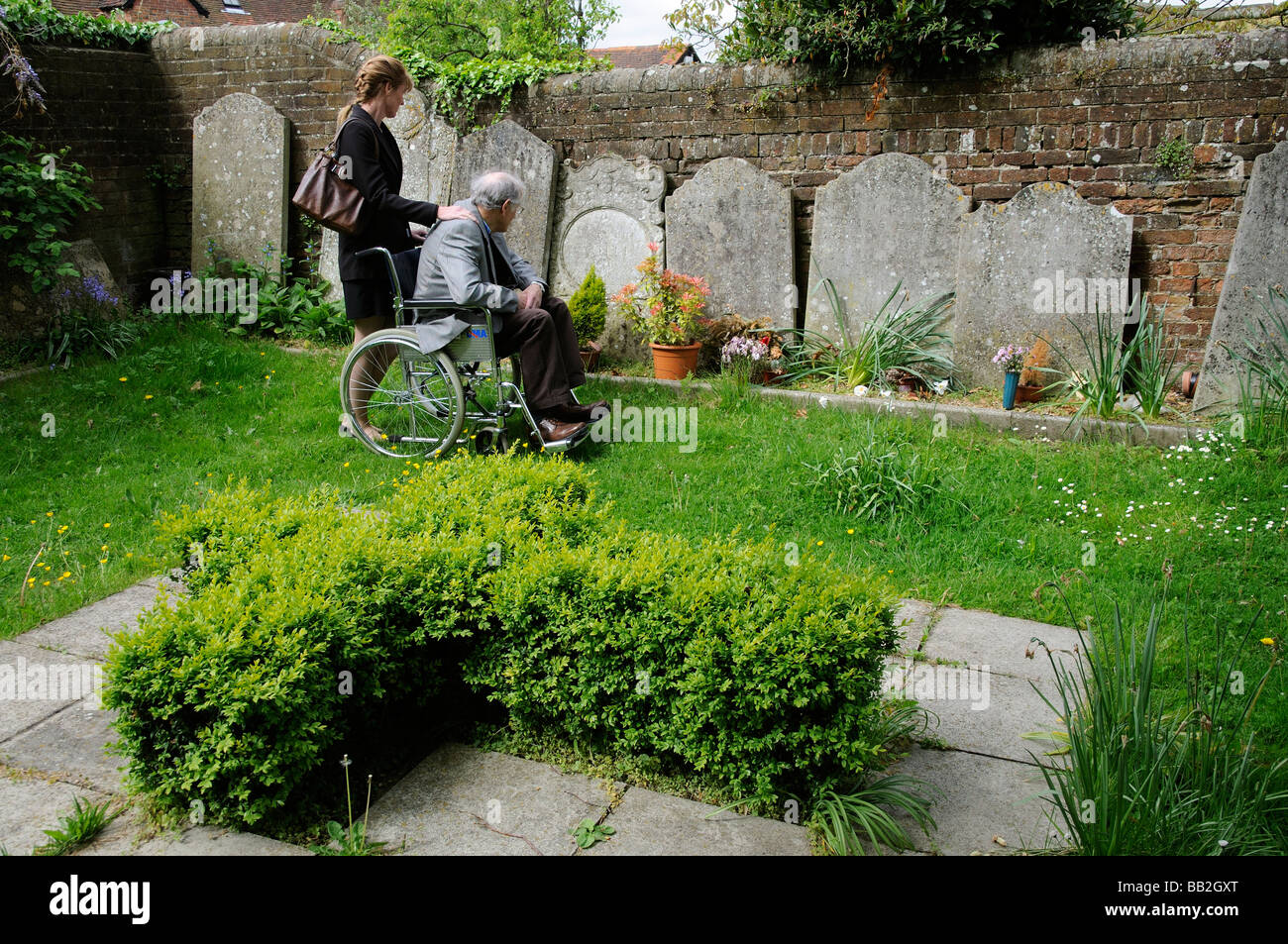 Elderly man in wheelchair being pushed around a graveyard by his female carer Stock Photo