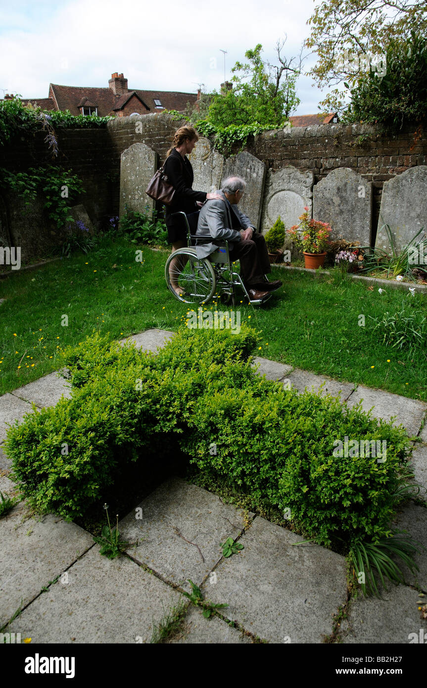 Elderly man in wheelchair being pushed around a graveyard by his female carer Stock Photo