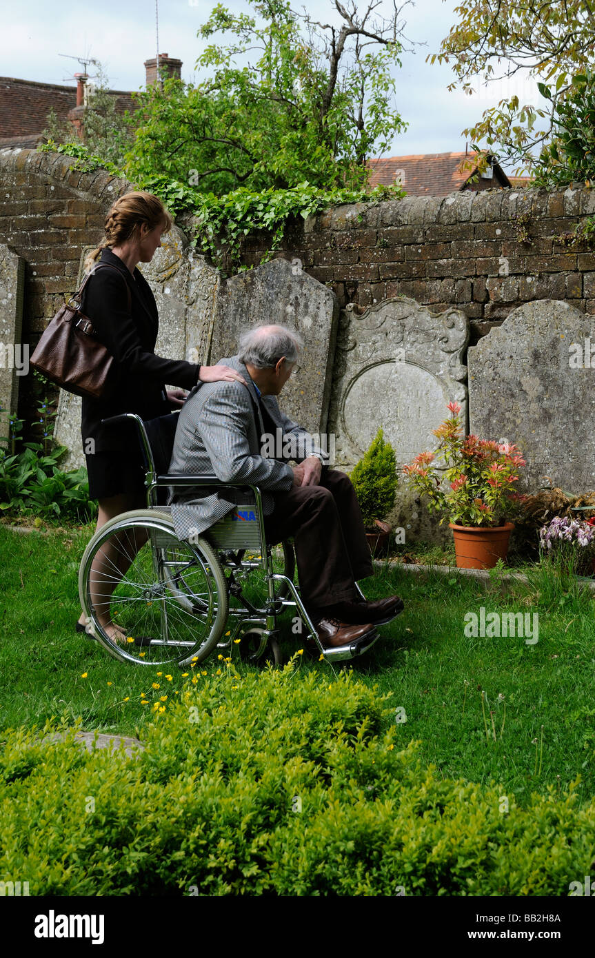 Elderly man in wheelchair being pushed around a graveyard by his female carer Stock Photo