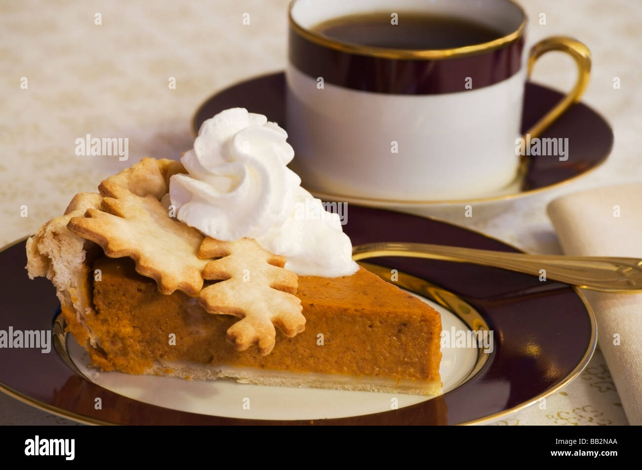 Pumpkin pie garnished with pastry leaves and whipped cream is served with a cup of coffee Stock Photo
