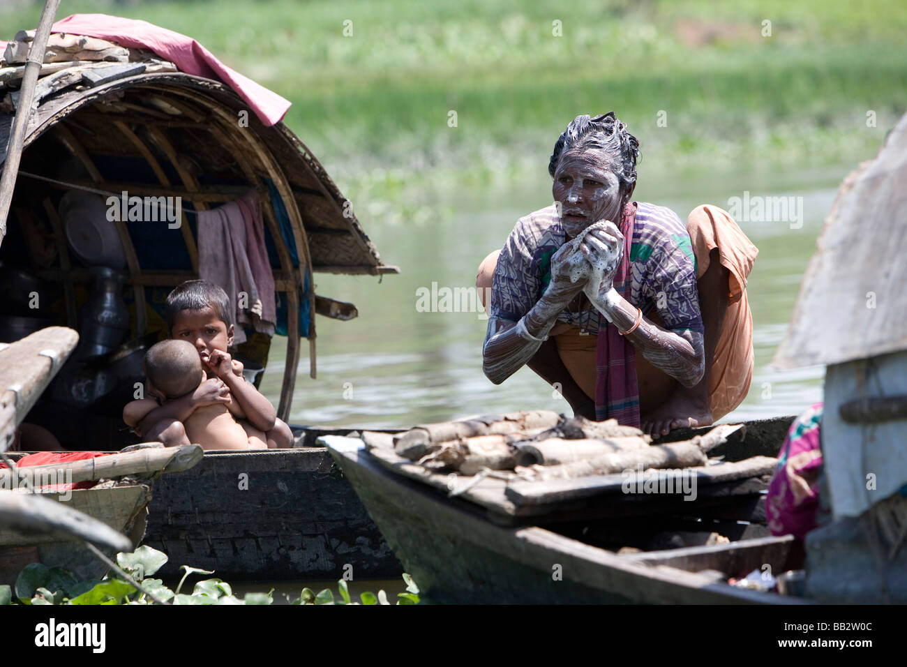 Daily Life in Bangladesh; A woman washes with river water while her children look on from their boat. Stock Photo