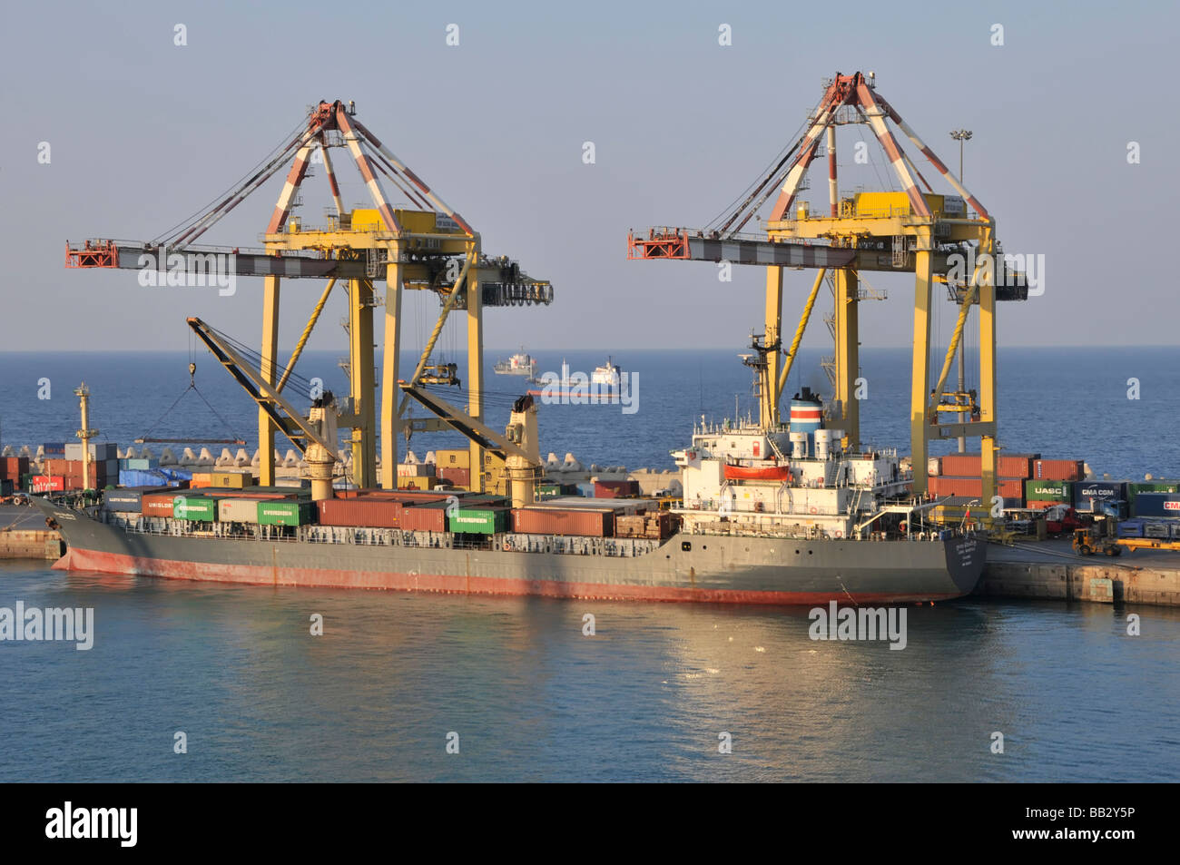 Shipping container ship cranes unloading at Muscat Port Sultan Qaboos Muttrah in Oman with shipping in the Gulf of Oman beyond Middle East Stock Photo