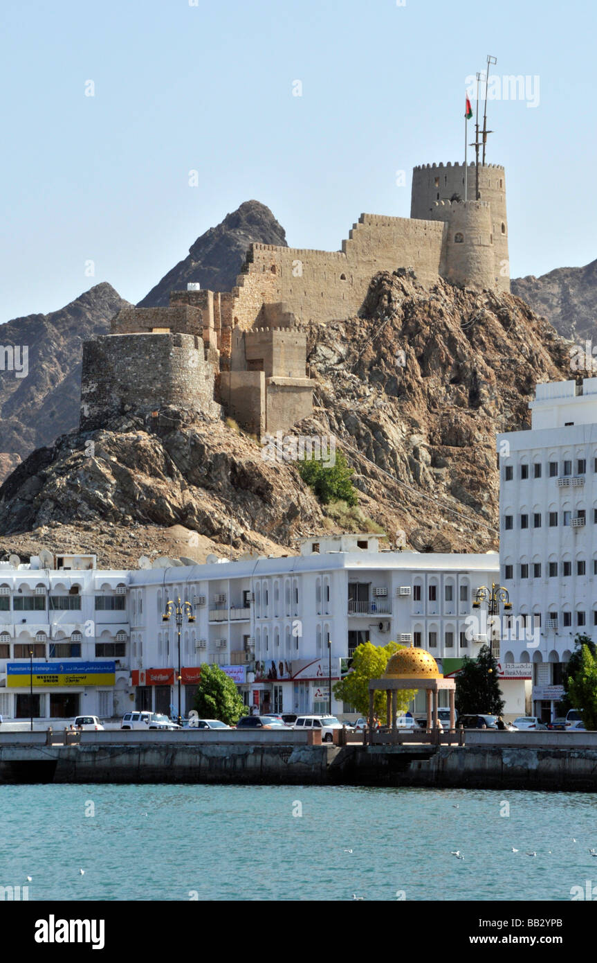 Historical Muttrah Muscat Fort on hillside above harbour waterfront & modern buildings along the Coniche promenade road Oman Gulf of Oman Middle East Stock Photo