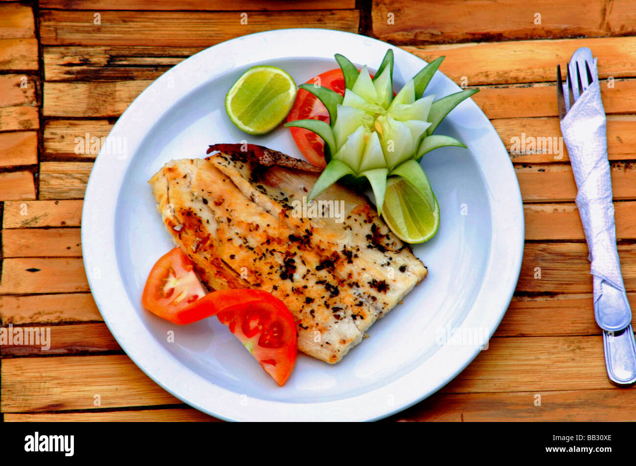 Plate of delicious healthy cuisine containing tropical fish fruit and vegetables served outdoors on a rustic bamboo table Stock Photo