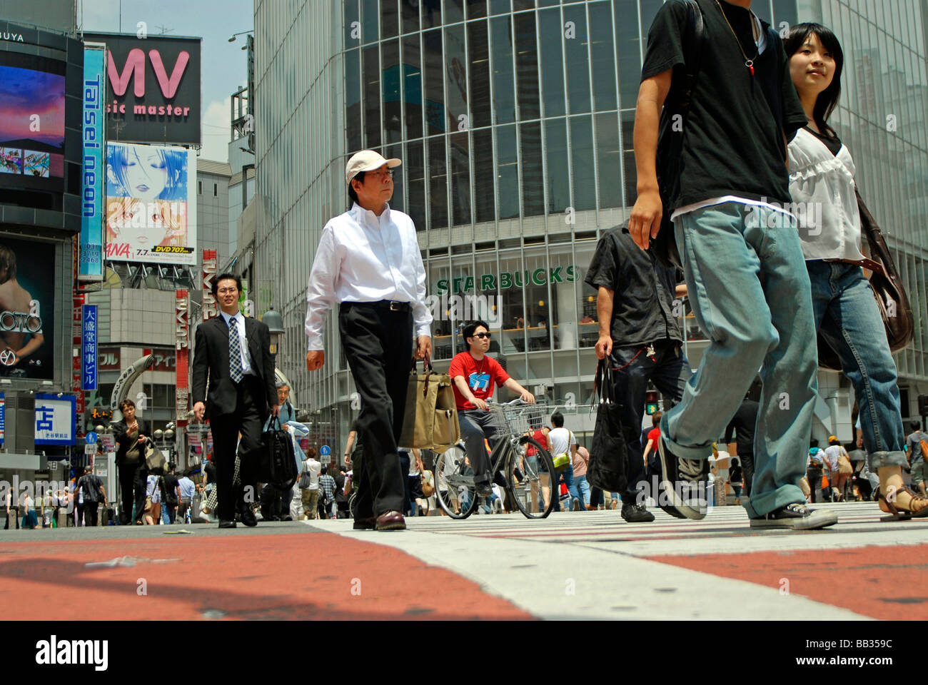 JAPAN, Tokyo. Japanese pedestrains crossing the street, a Starbucks and huge TV screens in the background Stock Photo