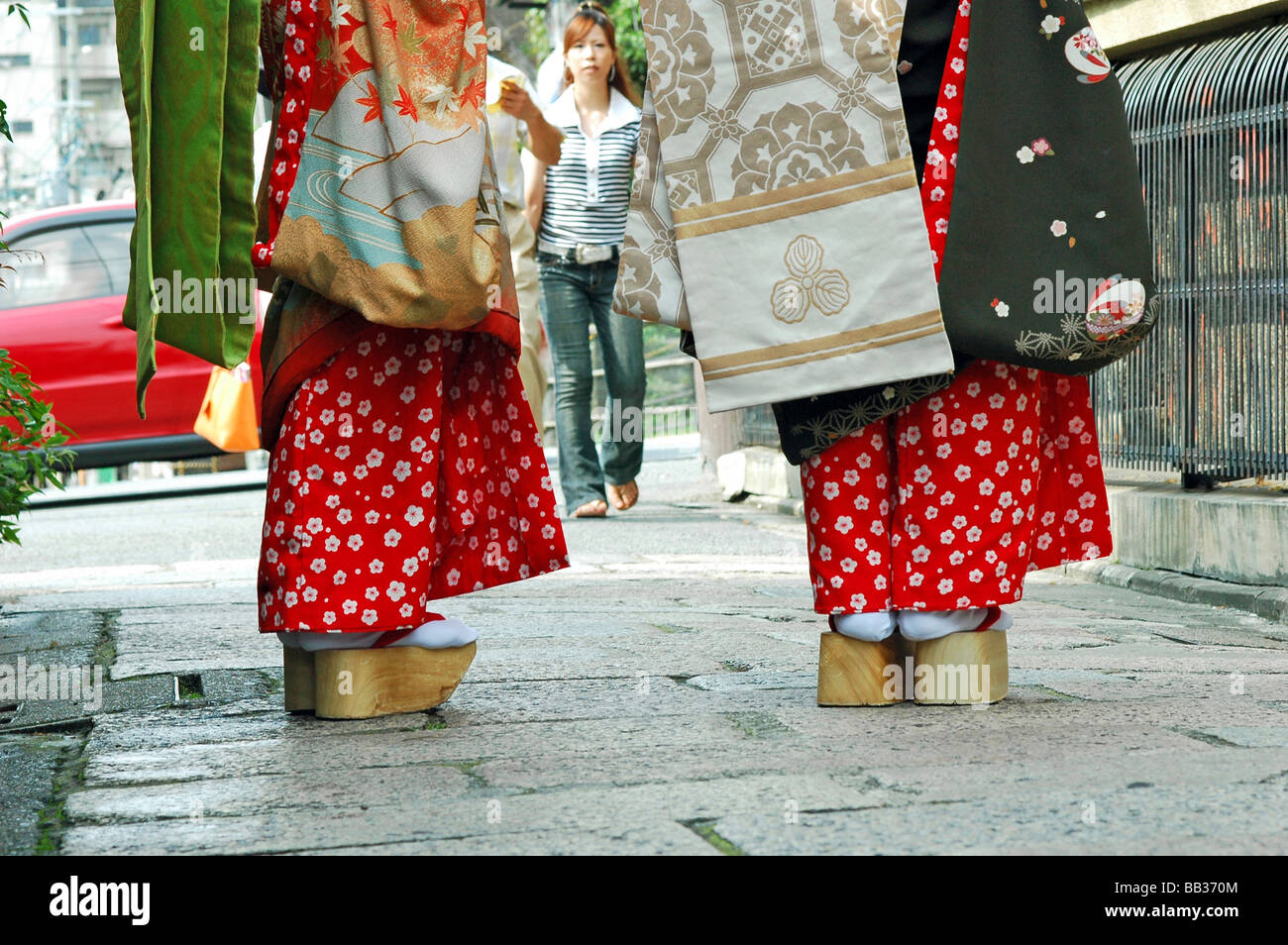 JAPAN, Kyoto. Two geishas standing in the street, wearing their traditional clothing and thick wooden sole sandals Stock Photo