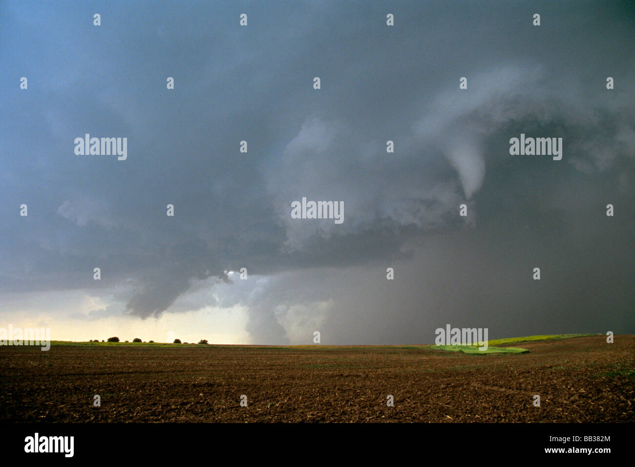 A funnel cloud in the foreground with a large tornado on the ground at the rear centre of the image. Kansas, USA Stock Photo
