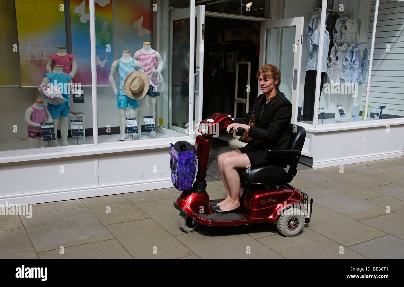 Female mobility scooter driver driving in town centre window shopping