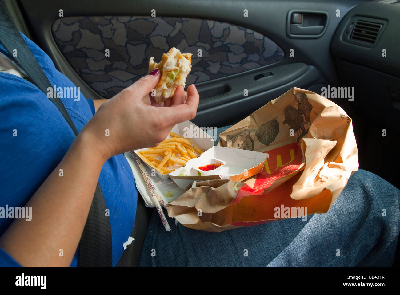 A woman eating a mcdonalds (fast food) inside a car with a chicken burger,fries and tomato ketchup in the uk Stock Photo