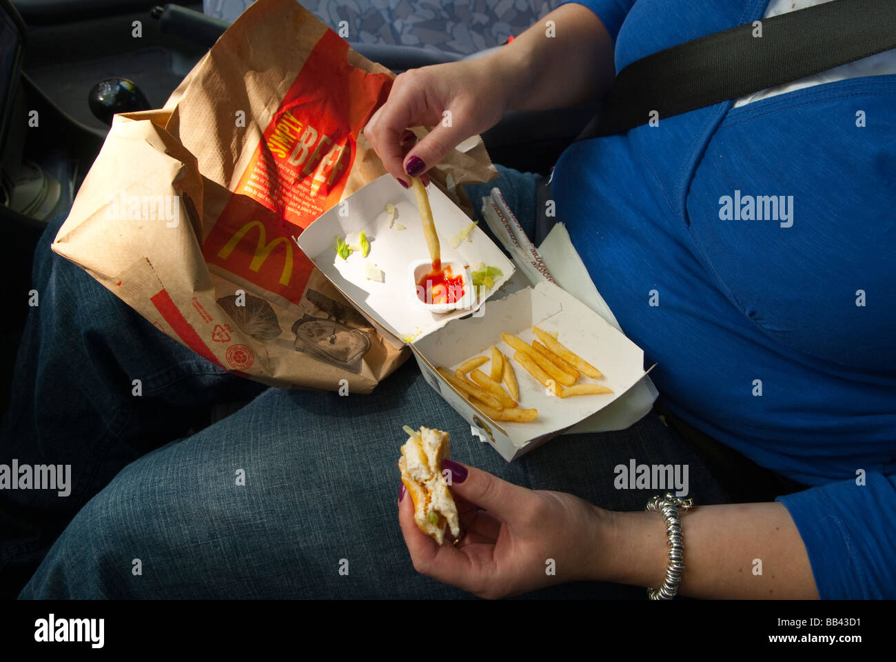 A woman eating a mcdonalds (fast food) inside a car with a chicken burger,fries and tomato ketchup in the uk Stock Photo
