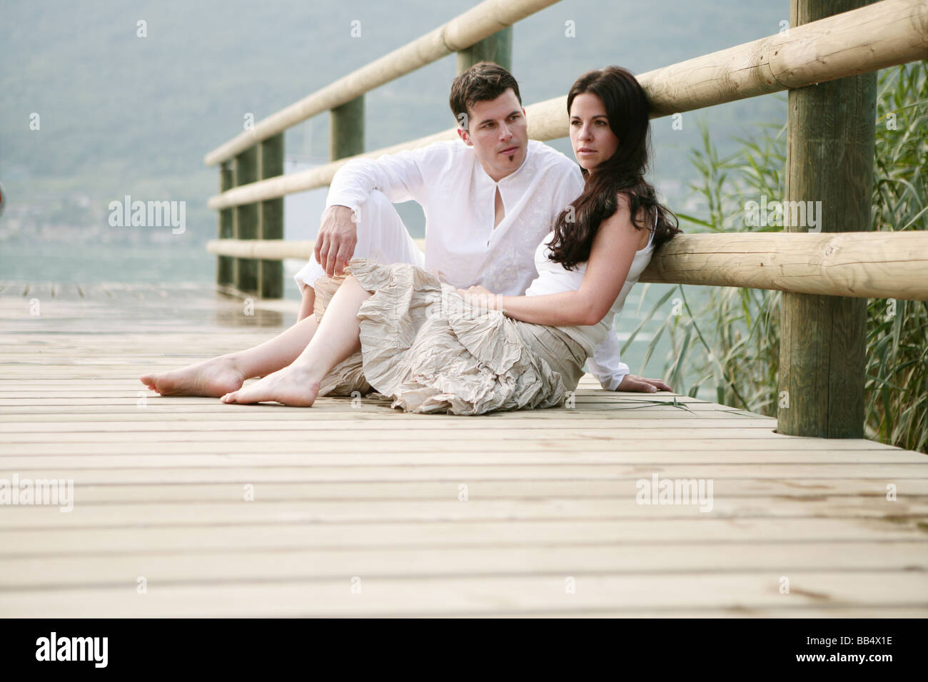 a couple sitting on a jetty at the lakeside Stock Photo
