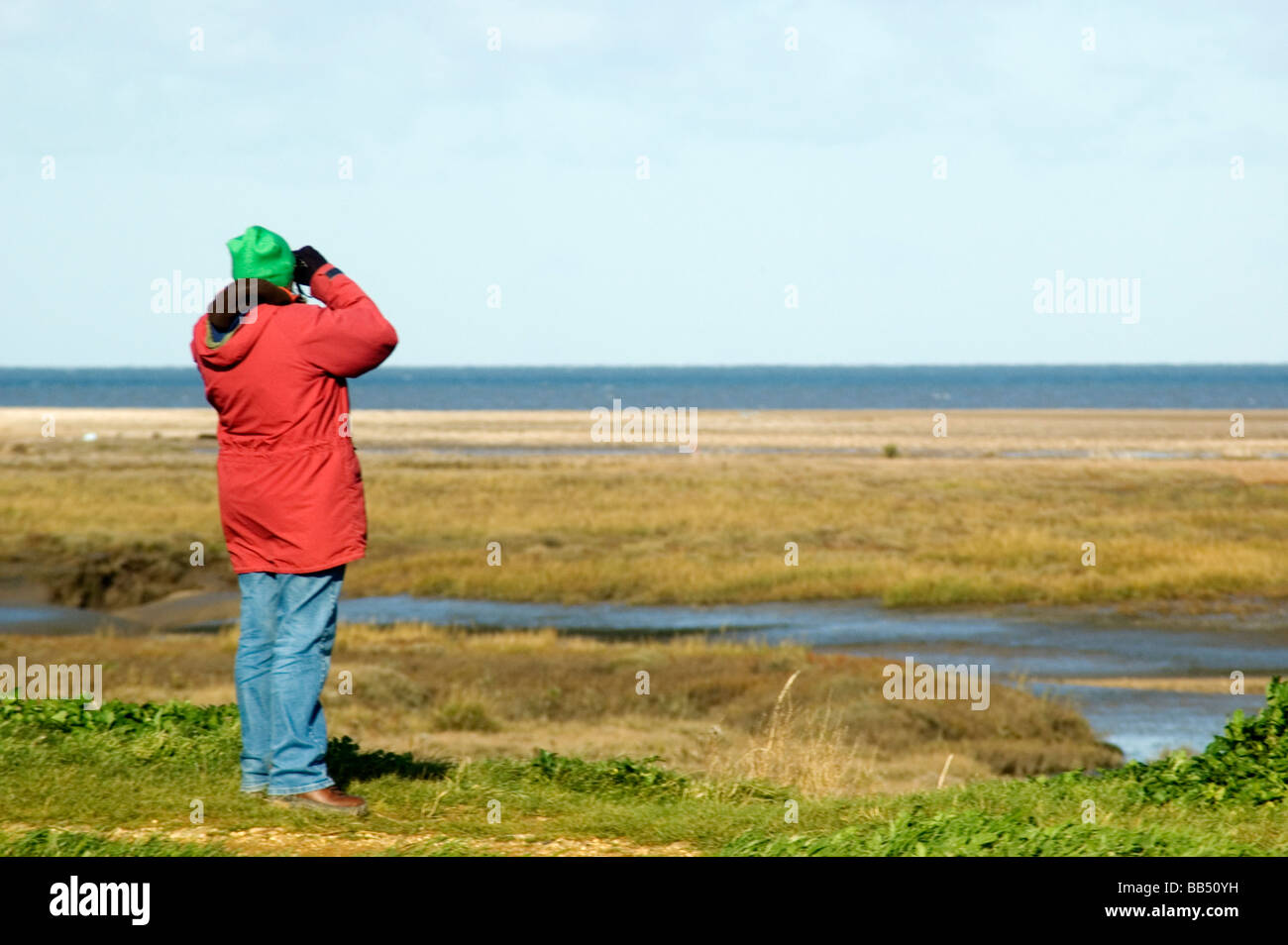 Female birdwatcher looking through binoculars on the North Norfolk coast. Stock Photo