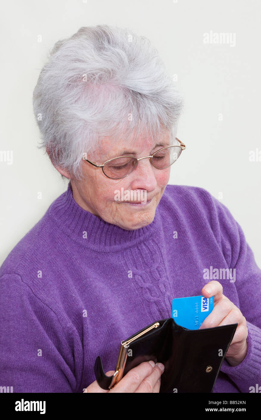 Elderly senior woman OAP lady removing a Visa debit card from a purse and looking serious. England UK Britain Stock Photo