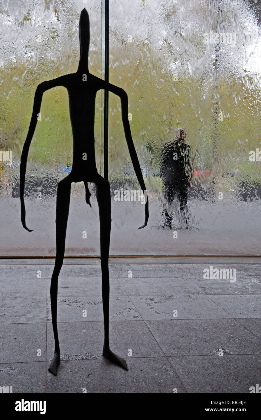 Metal sculpture human stick figure inside Victoria National Gallery Melbourne Australia with glass wall of running water Stock Photo