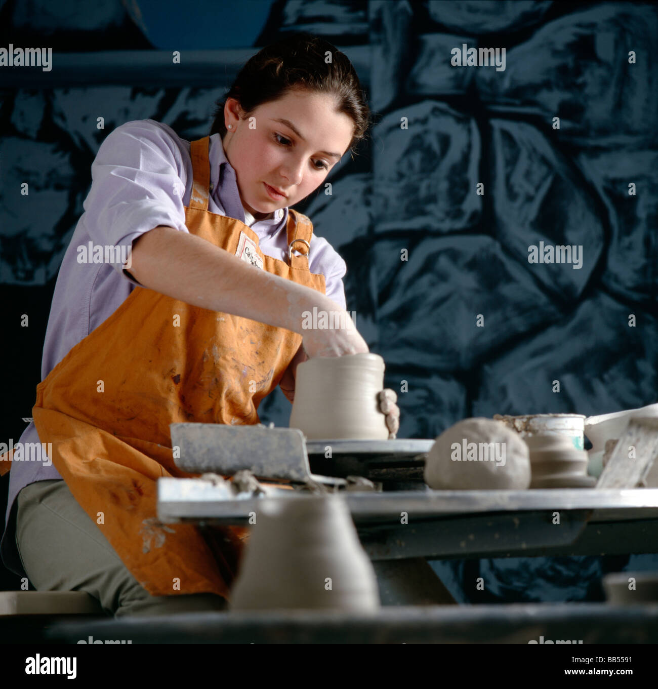 Teenage girl shaping pottery on a pottery wheel in a high school art class. Stock Photo