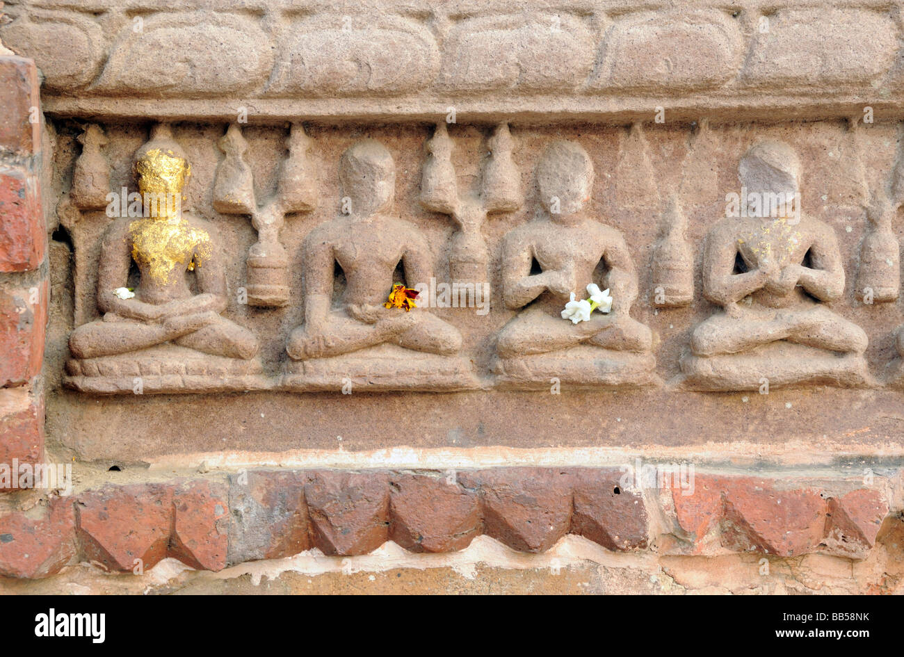 Row of small stone carved Buddhas defaced by time and vandals. They are decorated with flowers and one is covered with gold leaf Stock Photo
