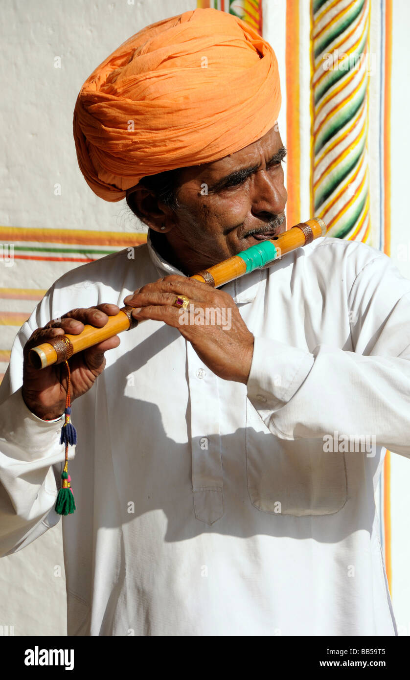 A  man with a moustache and an orange turban plays a bamboo flute Stock Photo