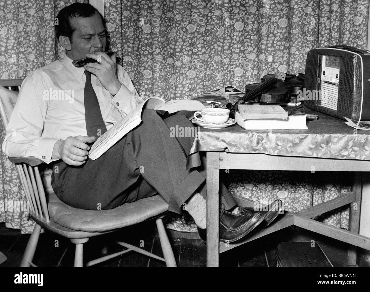 Deltgen, Rene, 30.4.1909 - 29.1.1979, Luxembourgian actor, half length, in his flat, sitting at table, reading script, playing harmonica, late 1950s, Stock Photo